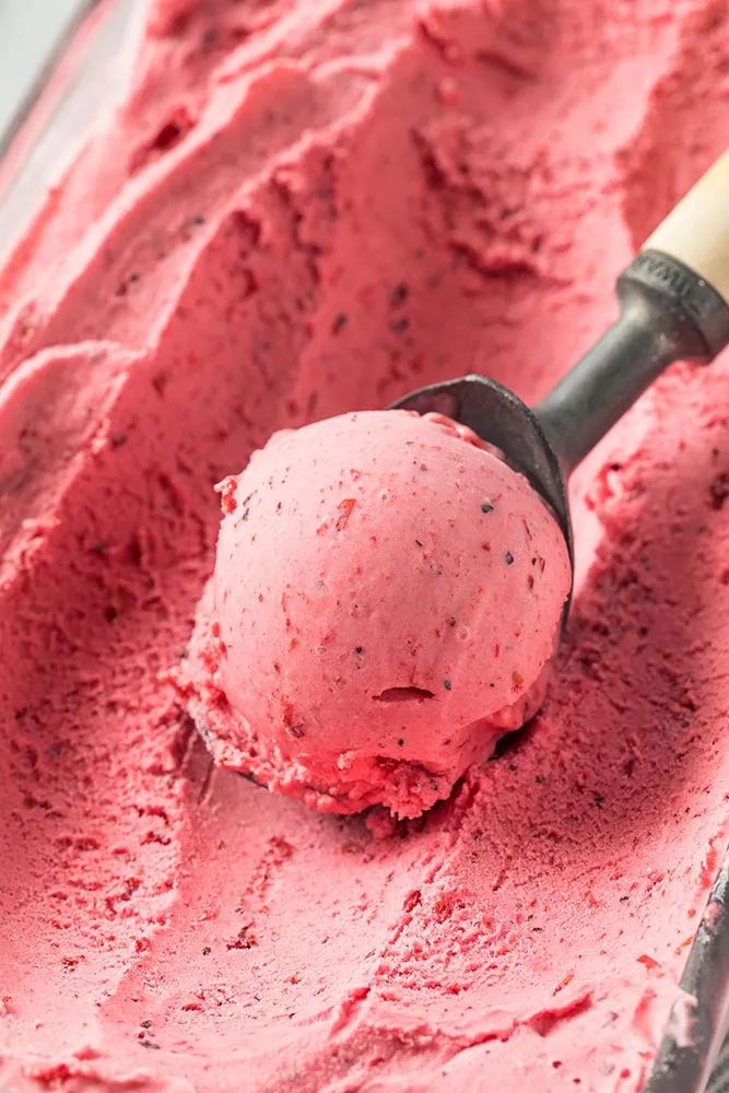 A scooper taking a scoop of strawberry sorbet