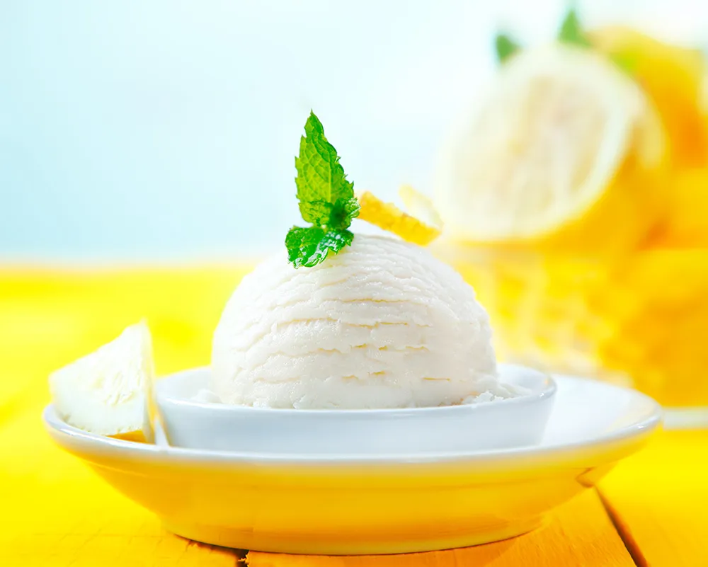 A single scoop of lemon sorbet sitting on a yellow table with a sprig of mint on top